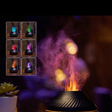 An elegant black diffuser sits on the table with a subtle LED light around the body, emitting puffs of scented smoke in the air. The top left corner has a panel that displays the LED Color variations.